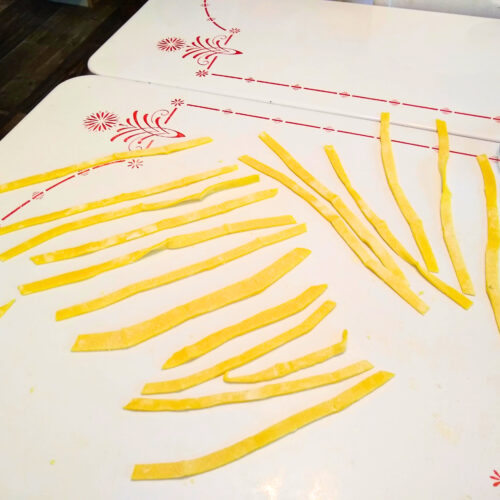 There are several noodles laid out on a table made from homemade pasta dough.