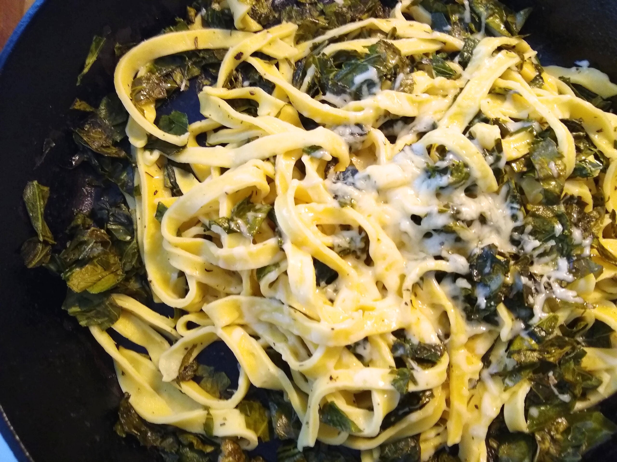 This is a cast iron skillet with homemade pasta topped with greens, herbs, butter, and cheese.