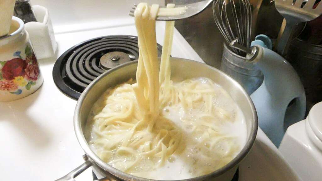sourdough pasta cooking in boiling water with a fork holding some of the pasta up