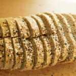 This is an overhead shot of the sourdough quinoa whole wheat sandwich loaf. It is sliced and topped with every bagel seasoning and is on a wooden cutting board.