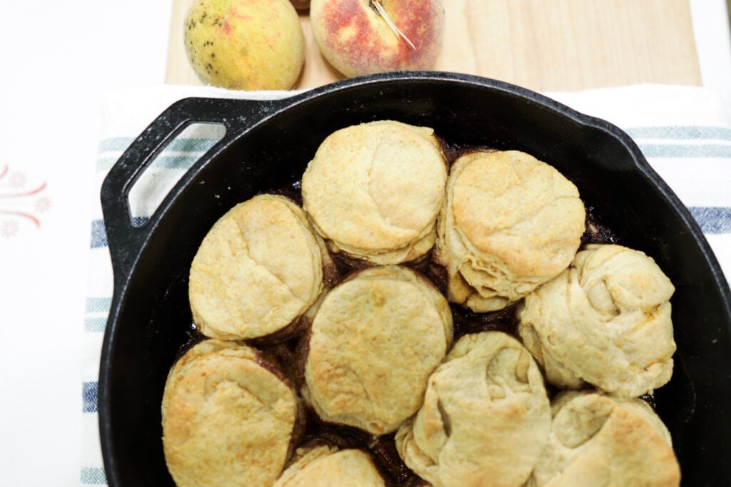 cast iron skillet with biscuits beside 2 peaches on a cutting board.