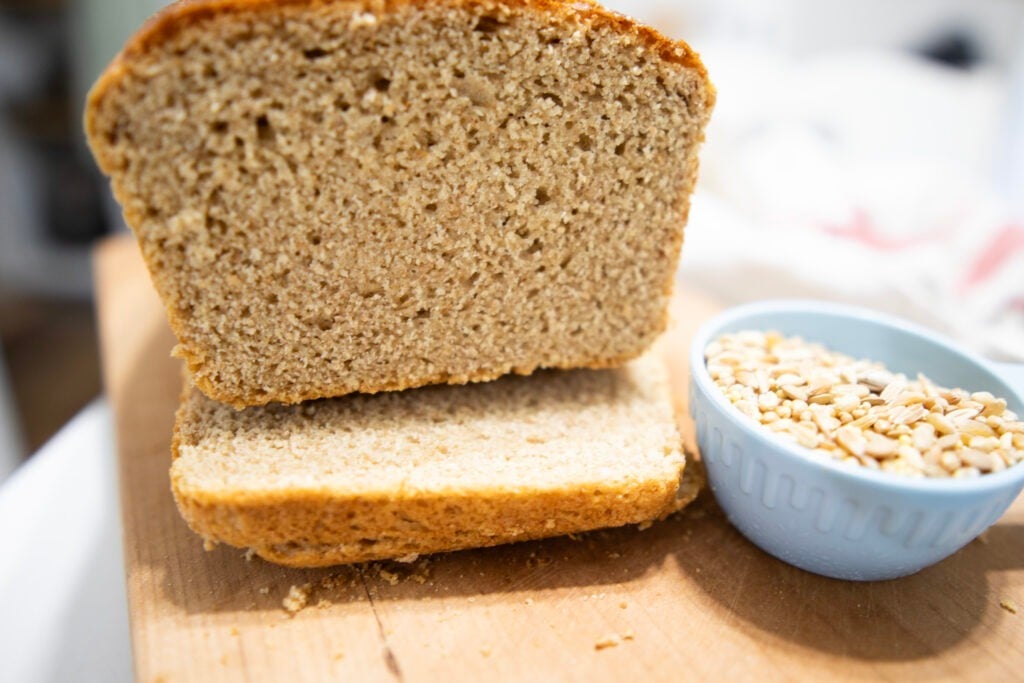 Sliced Ezekiel bread on a cutting board with Ezekiel mix in a cup beside the loaf of bread