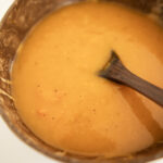 a wooden bowl with butternut squash soup and a wooden spoon