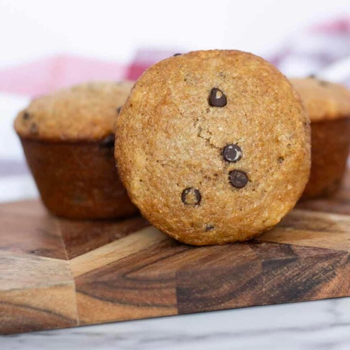 sourdough chocolate chip muffins on a cutting board with a red and white towel in the back ground.