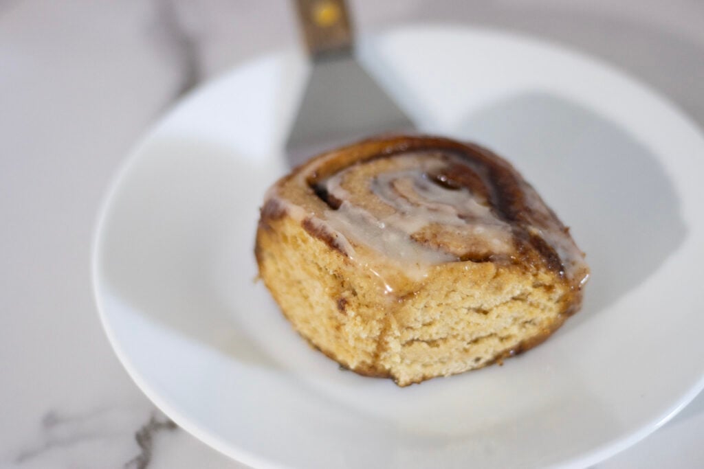 cinnamon roll on plate held by a spatula