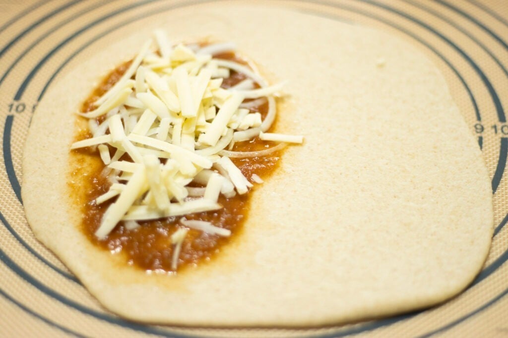 calzone dough rolled out in a circle with toppings on one side