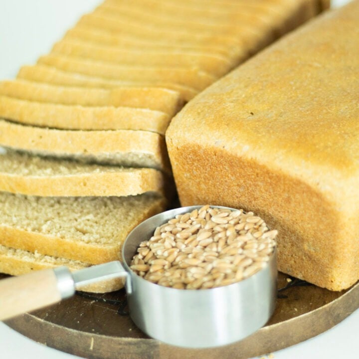 2 loaves of bread, one sliced with a cup of wheat berries in the foreground.