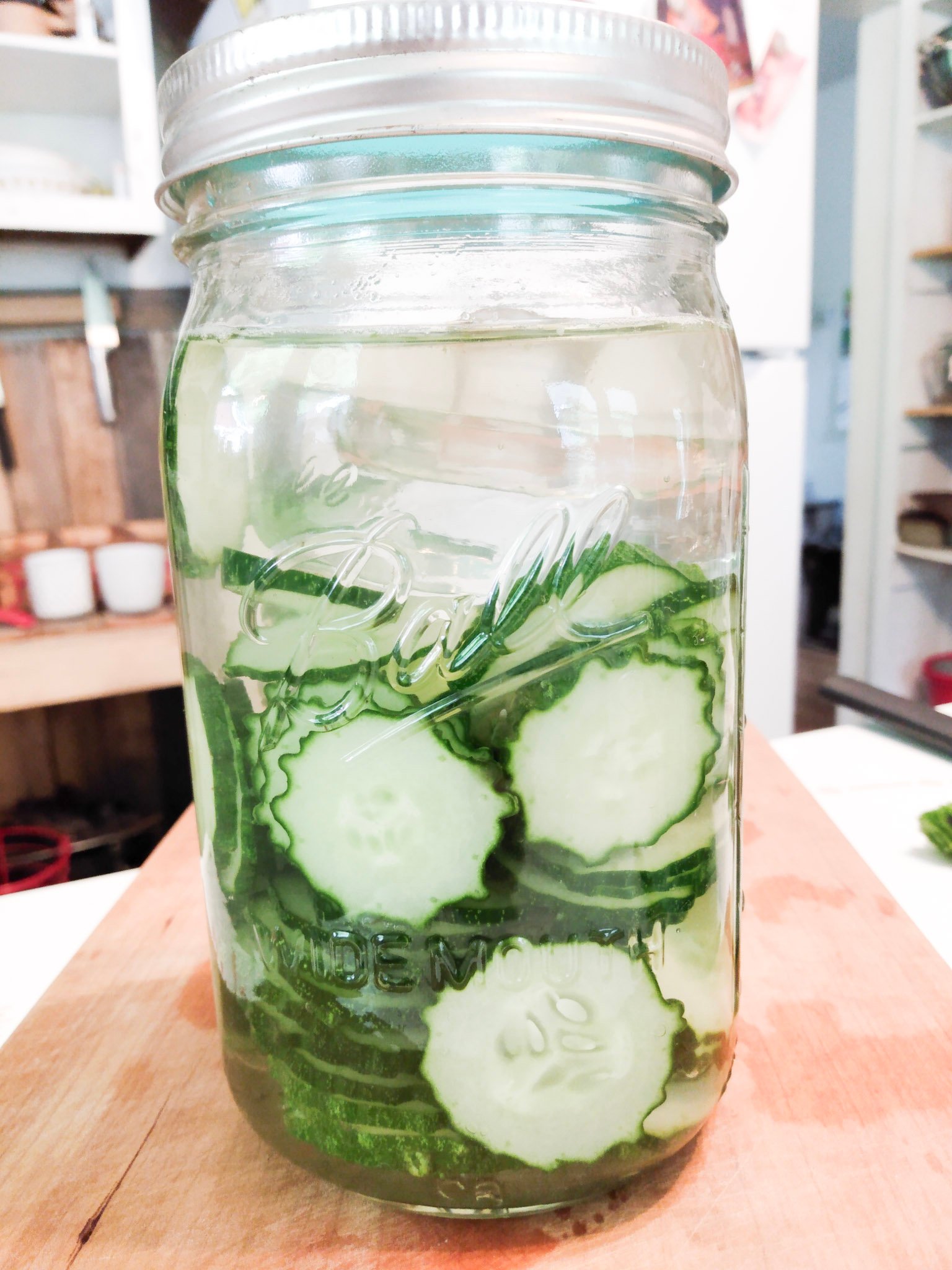 A jar of lacto fermented pickles in a quart jar sitting on a wooden cutting board.