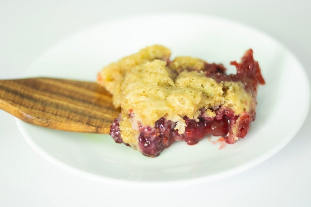 berry cobbler on a white plate. There is a wooden spatula as well