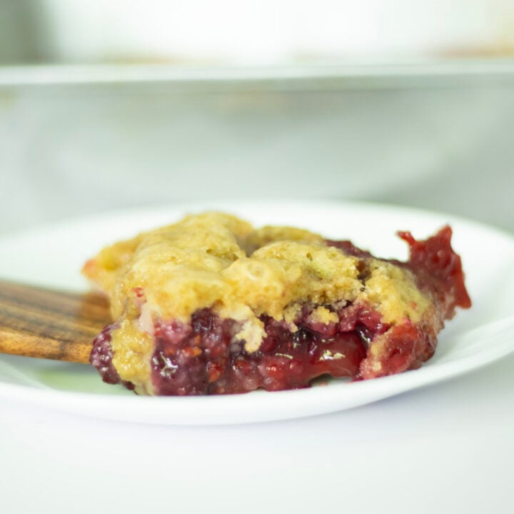 berry cobbler on a white plate with a wooden spatula underneath