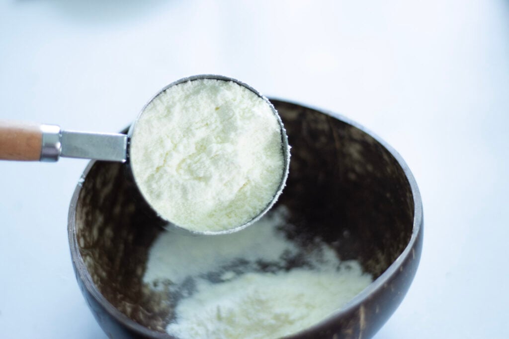 homemade powdered coffee creamer being poured from a measuring cup to a wooden bowl. 