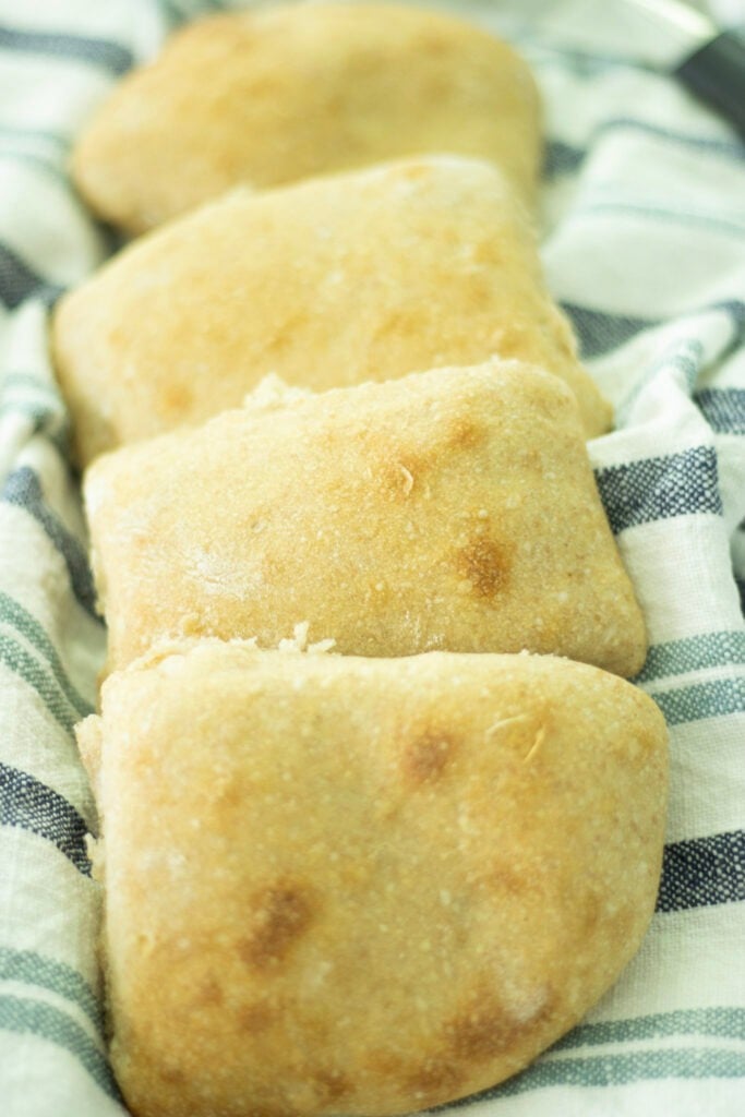 sourdough ciabatta rolls stacked on a blue and white towel