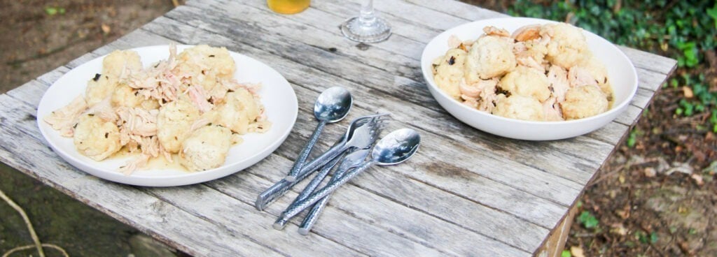 an outside table with 2 plates of chicken and dumplings with silver ware in between