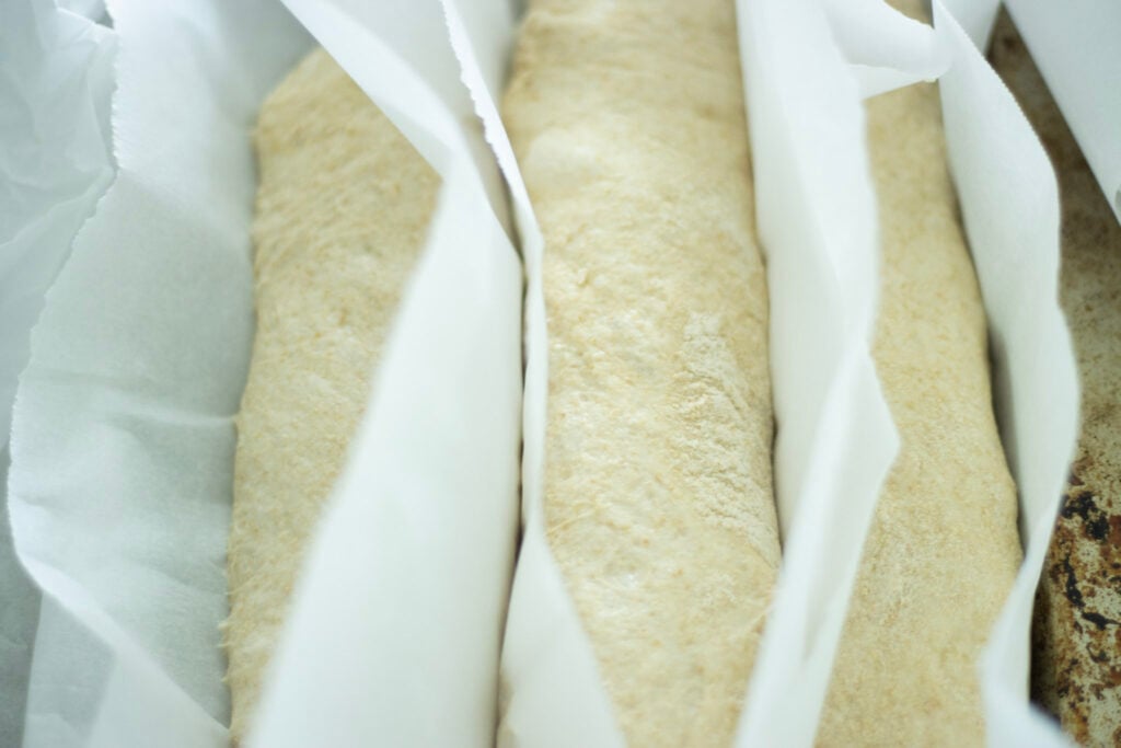 shaped sourdough baguette dough in parchment paper on a rising cloth