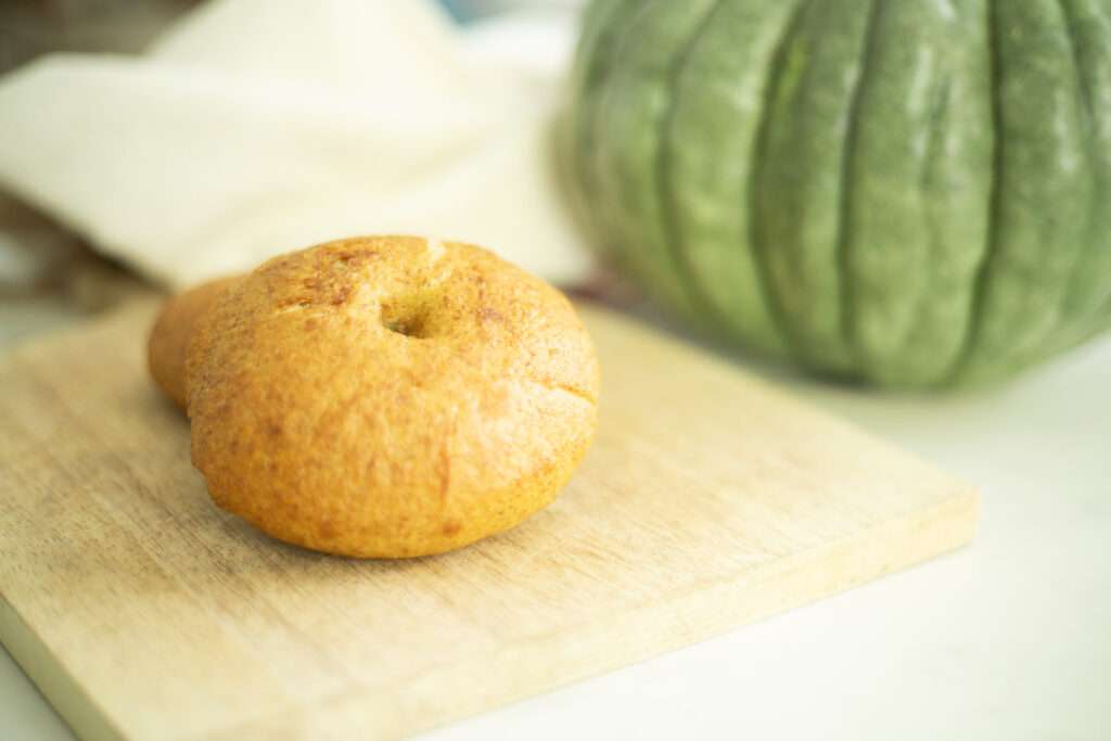 sourdough pumpkin bagel on a cutting board with a pumpkin in the background