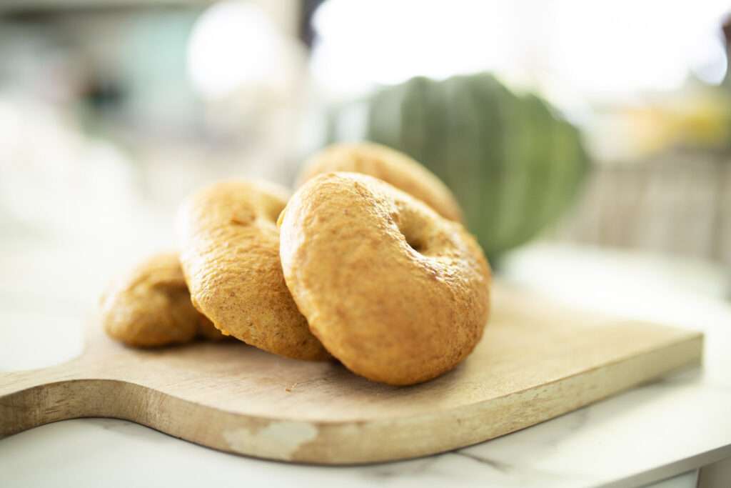 stack of sourdough pumpkin bagels on a cutting board with a pumpkin blurred in the background