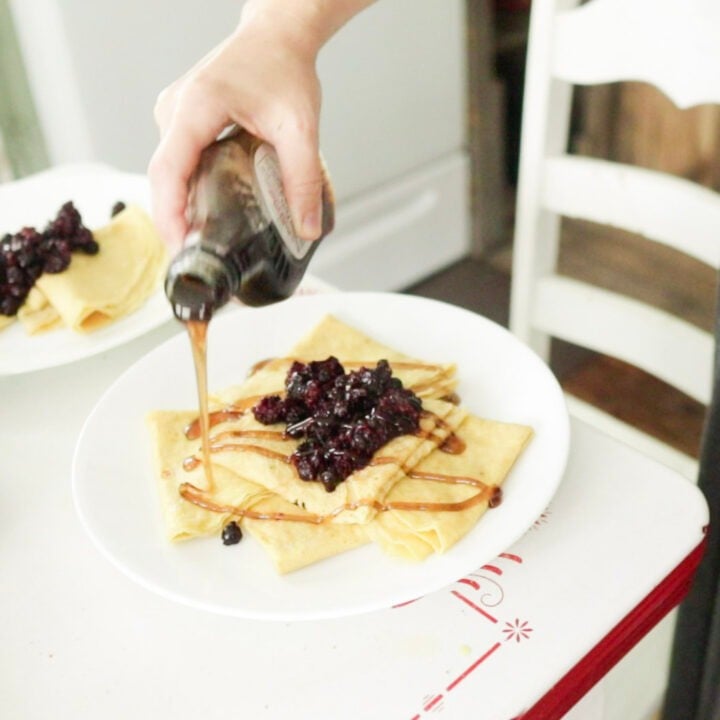 Pouring homemade pancake syrup over a plate of crepes
