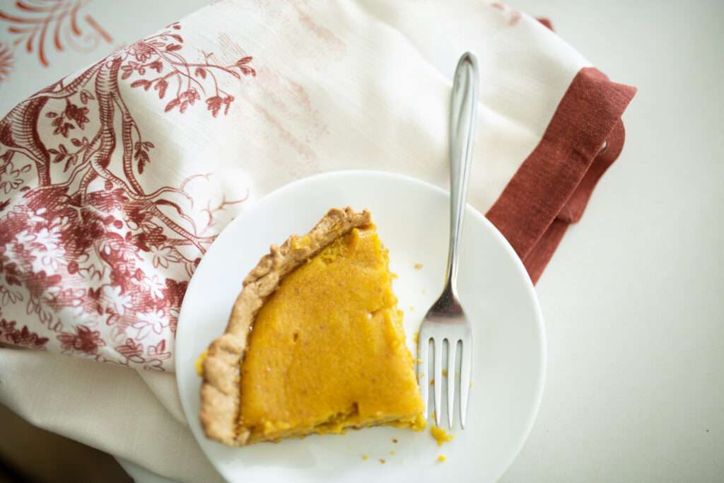 overhead shot of piece of sourdough pumpkin pie on white plate with red and white towel in background