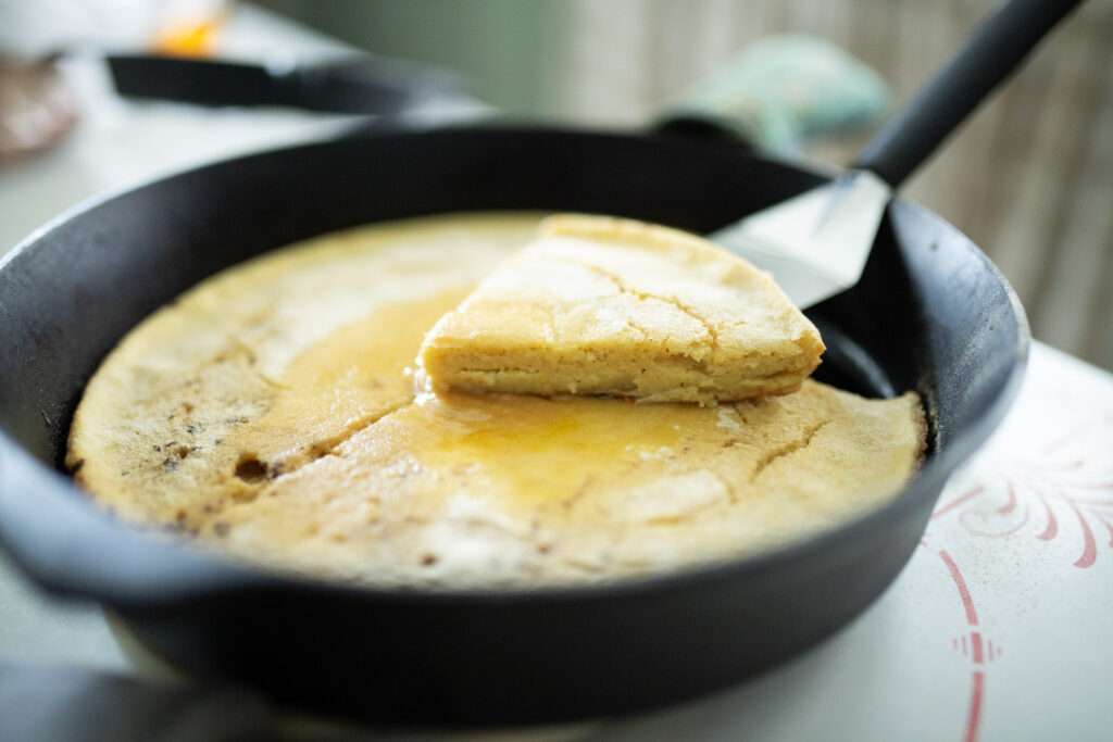 sourdough german pancake in cast iron skillet with one slice cut out and lifted up