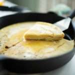sourdough german pancake in cast iron skillet with one slice cut out and lifted up