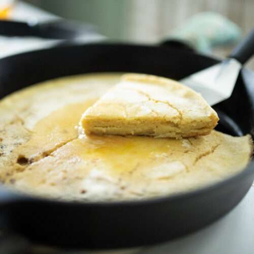 sourdough german pancake in cast iron skillet with one slice cut out and lifted up
