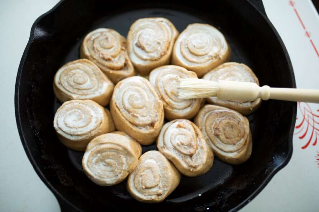 cast iron skillet with sourdough pumpkin cinnamon rolls brushed with milk