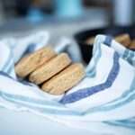 side view of 3 einkorn biscuits on a blue and white towel. A skillet of biscuits is in the background