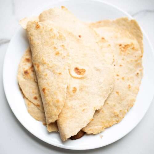 a white plate with fresh milled tortilla. a few are folded on top