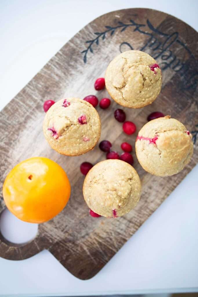 An overhead photo of 4 sourdough discard cranberry orange muffins on a cutting board with a few cranberries and an orange