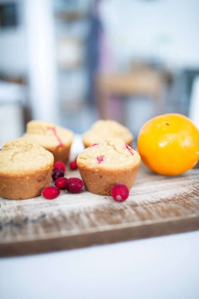This is a side view of sourdough cranberry orange muffins with cranberries and an orange on a board.