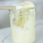 Side view of a mason jar of homemade mayonnaise with a spatula on top.