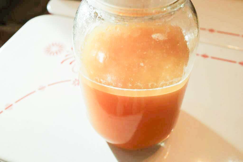 Golden bone broth in a glass mason jar on a white table.