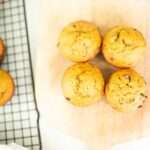 Overhead shot of 4 spelt pumpkin chocolate chip muffins on a board with more on a cooling rack besides.