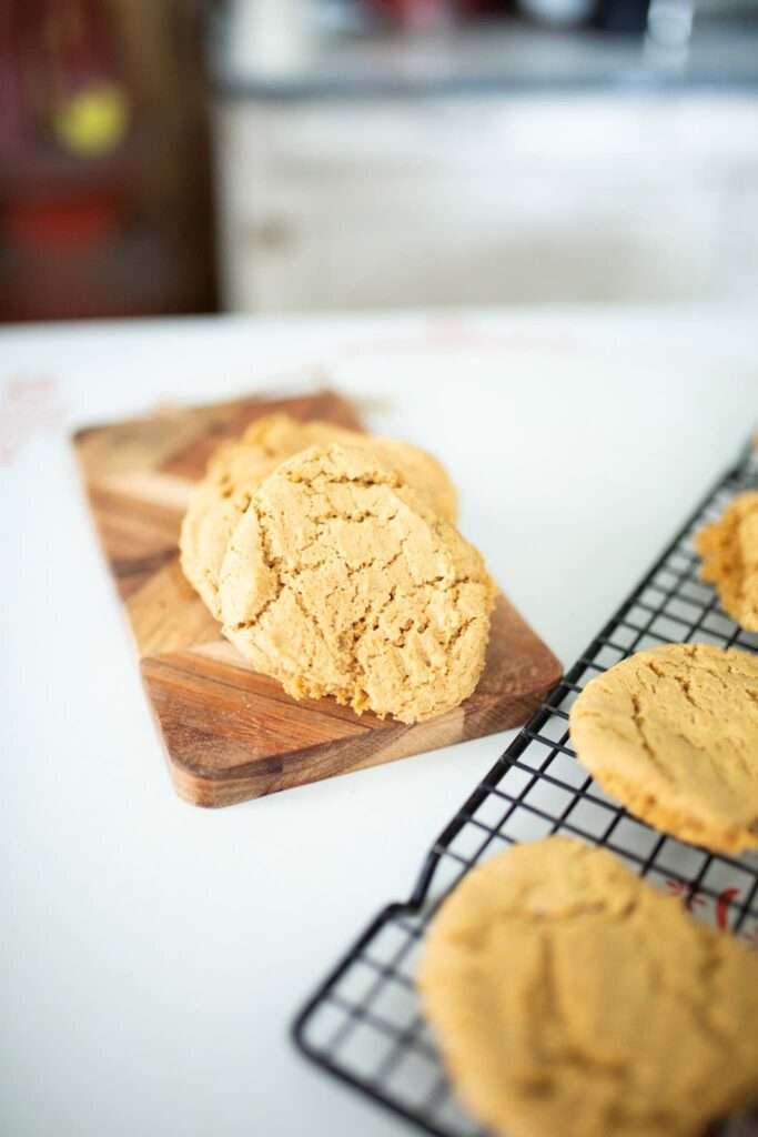 A stack of Einkorn peanut butter cookies on a board behind a wire rack with more cookies.