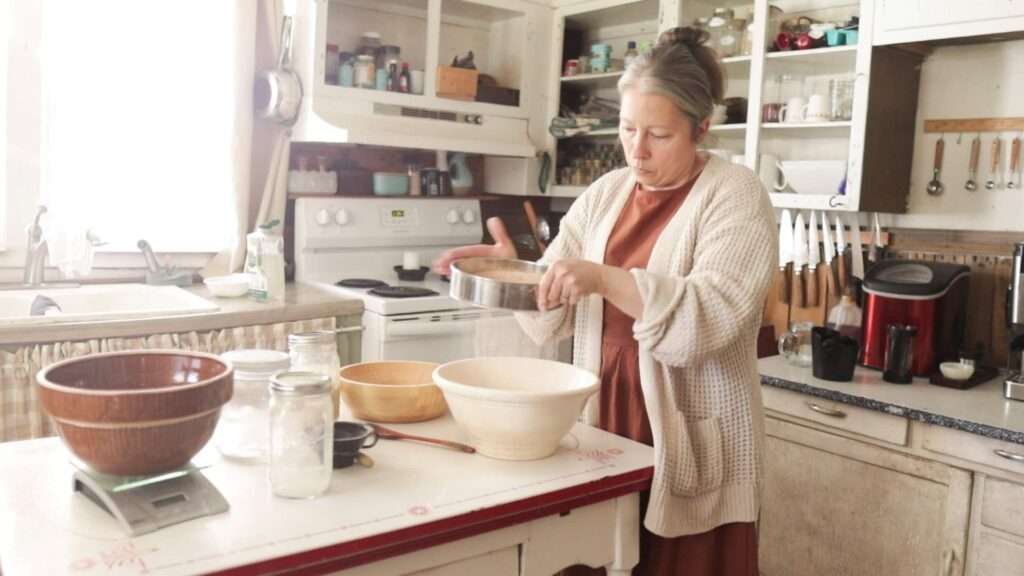 Lady in white sweater holding a sifter over a white bowl