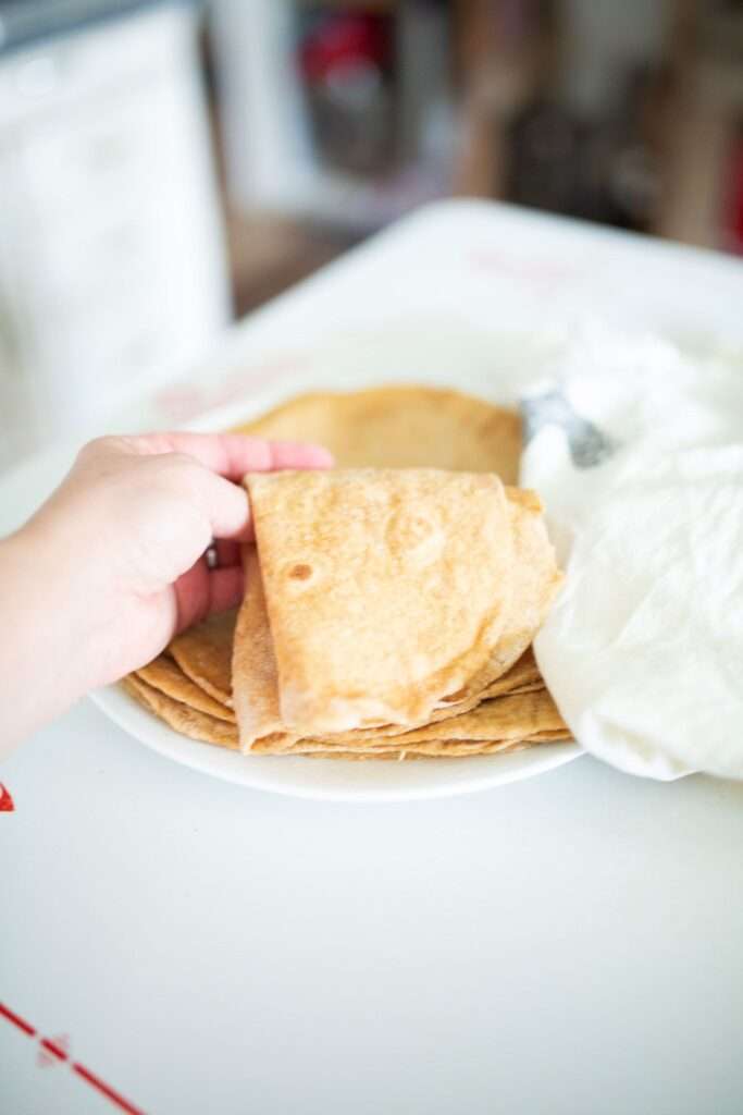 There is a hand folding a sourdough einkorn tortilla over a plate of tortillas.