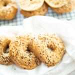 3 sourdough einkorn bagels on a white towel with more bagels behind on a wire rack.
