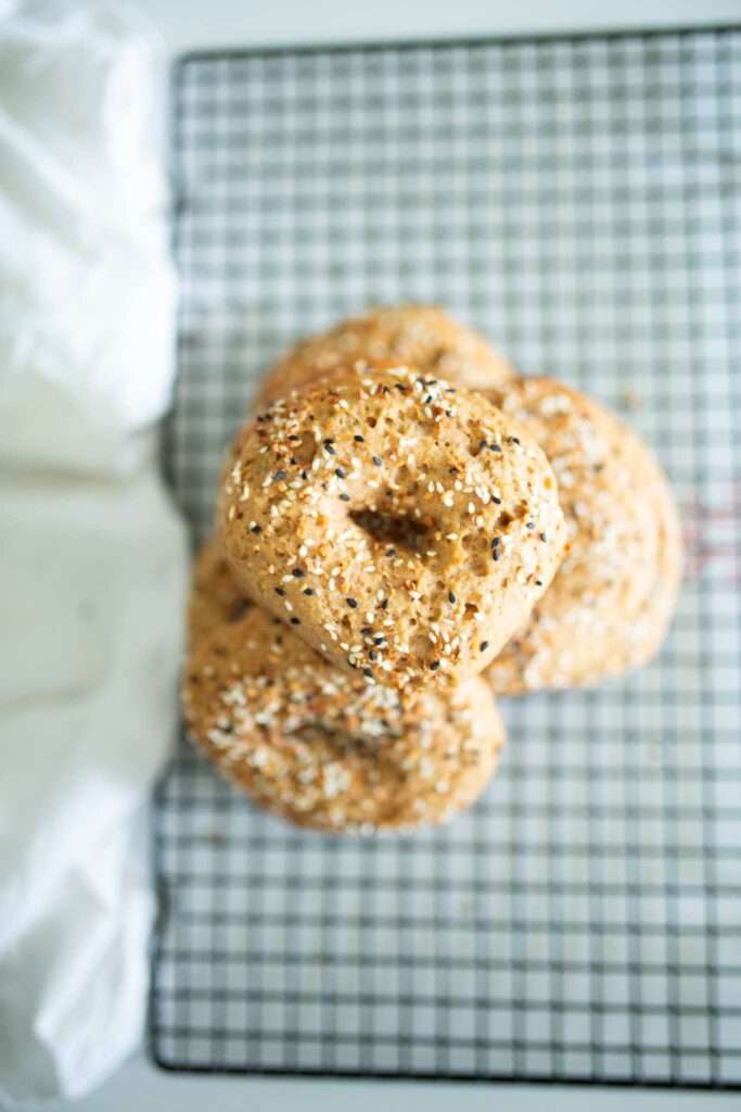 4 sourdough einkorn bagels stacked on a wire rack.