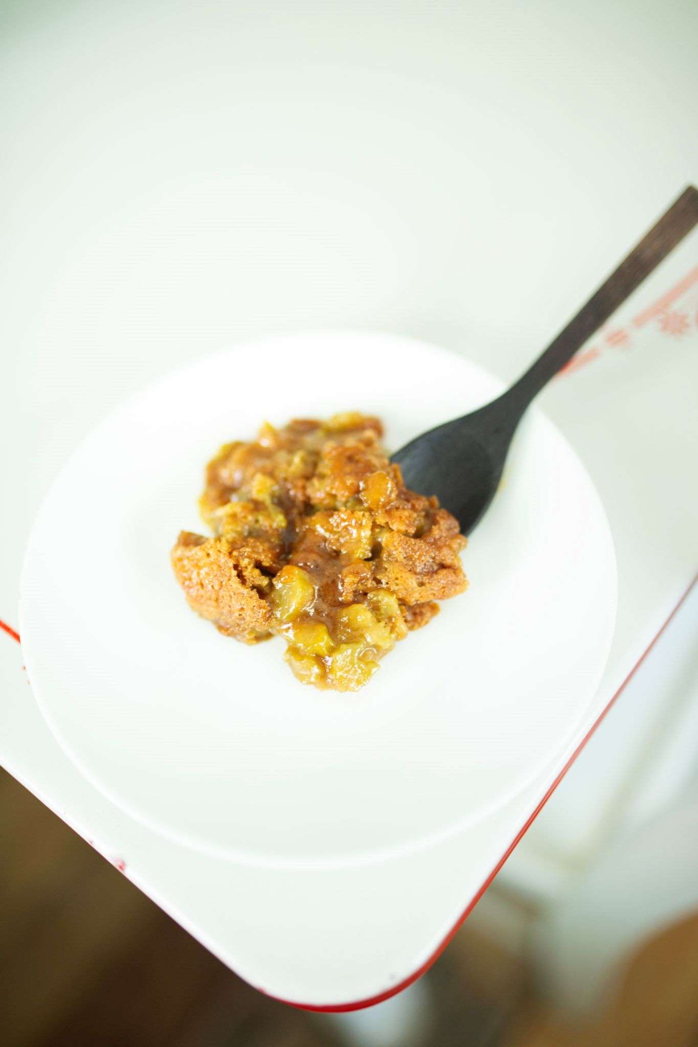 A serving of sourdough rhubarb cobbler on a white plate that is sitting on the corner of a table.