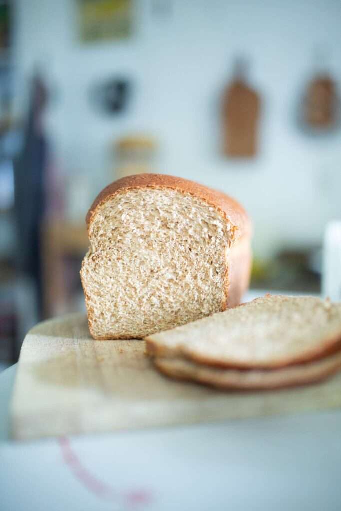 Loaf of spelt sandwich bread with 2 slices on a cutting board.