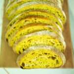 Turmeric sourdough bread sliced on a wooden cutting board.