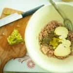 There is a small cutting board with jalapenos chopped beside a bowl with tuna, relish, and mayo.