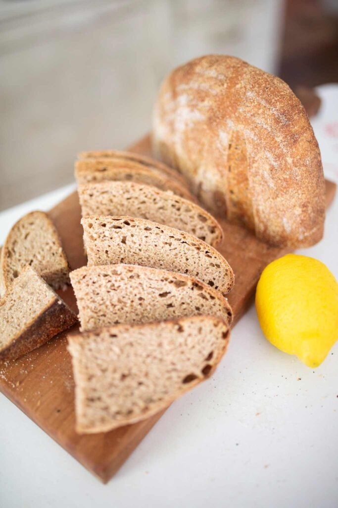 Slices of a loaf of sourdough lemon rosemary bread on a cutting board with a lemon beside.