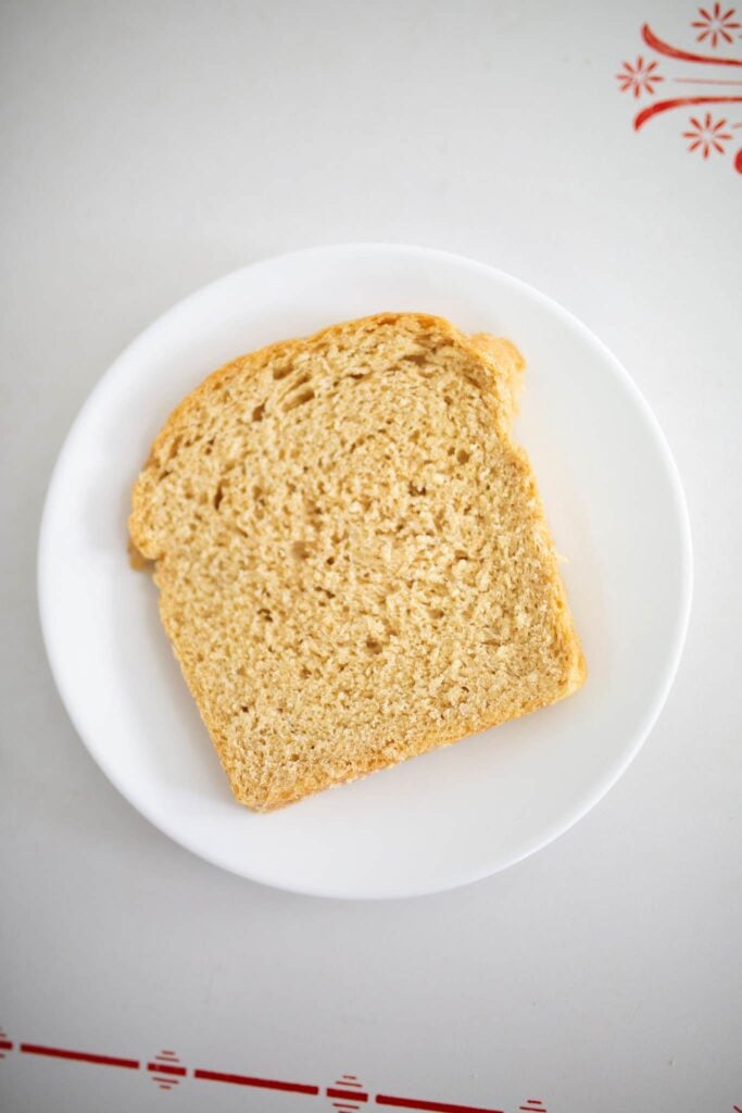 A slice of sourdough sandwich bread on a white plate sitting on a white table.