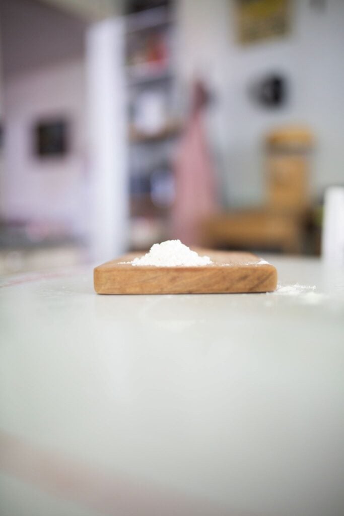 This is a side view of some all purpose flour on a wood cutting board sitting on a white table.