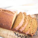 Side view of a loaf of golden brown banana bread that is halfway sliced through.