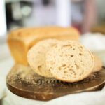 A sourdough hamburger bun and loaf of sandwich bread from the master sourdough dough recipe on a cutting board