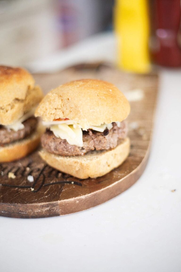 There are 2 hamburgers on sourdough kamut buns sitting on a wooden cutting board.