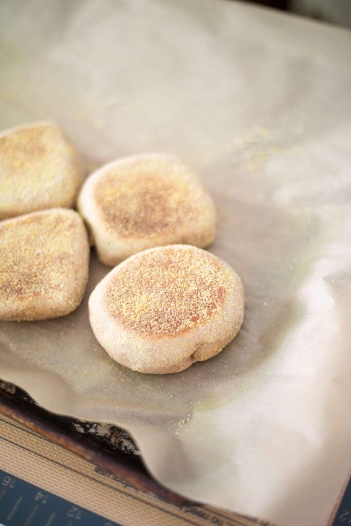 golden brown fresh milled english muffins on a piece of parchment paper.
