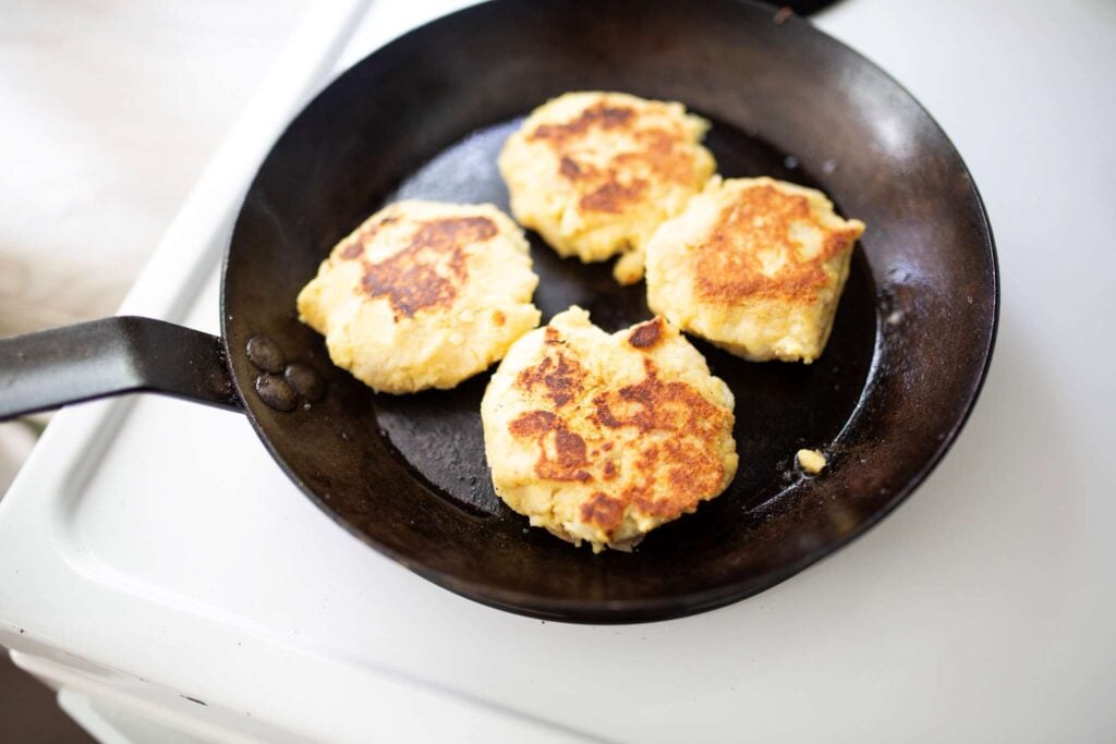 There are 4 golden brown potato cakes in a cast iron skillet.